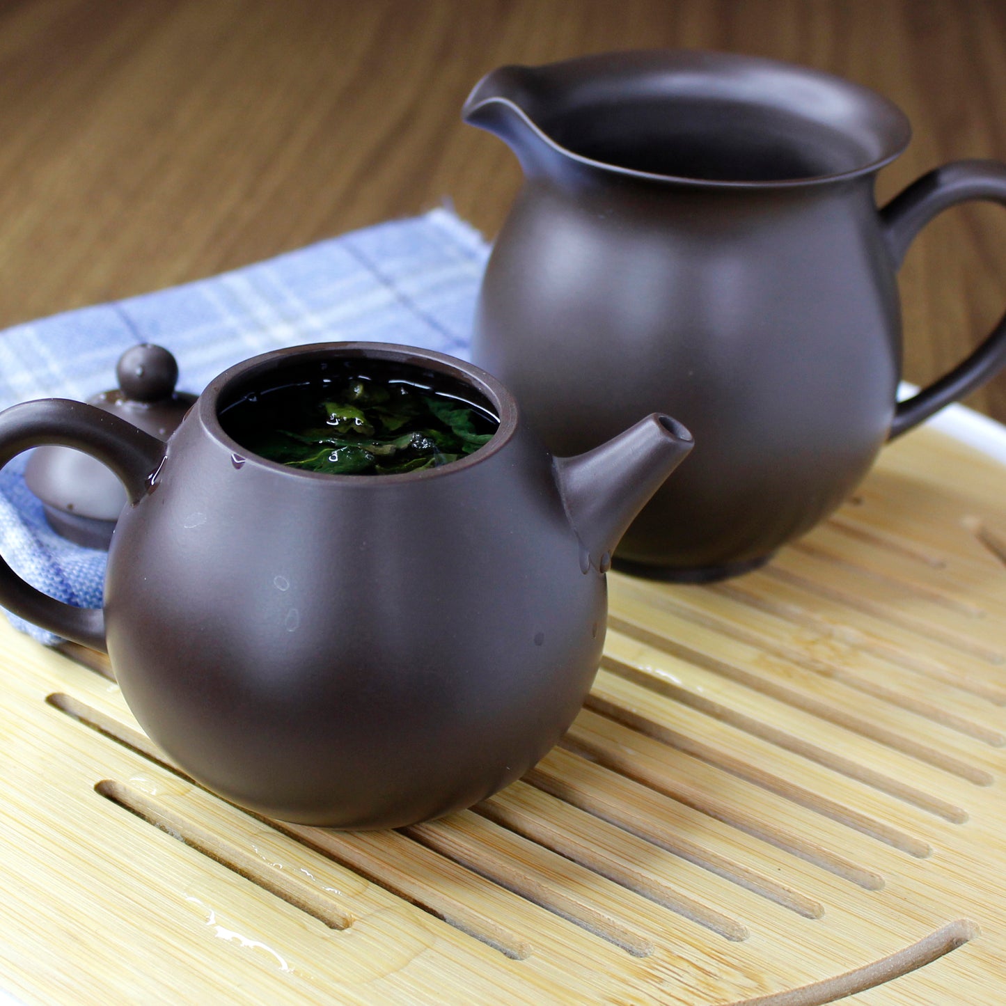 A clay teapot with tea in front of the Purple clay pitcher.