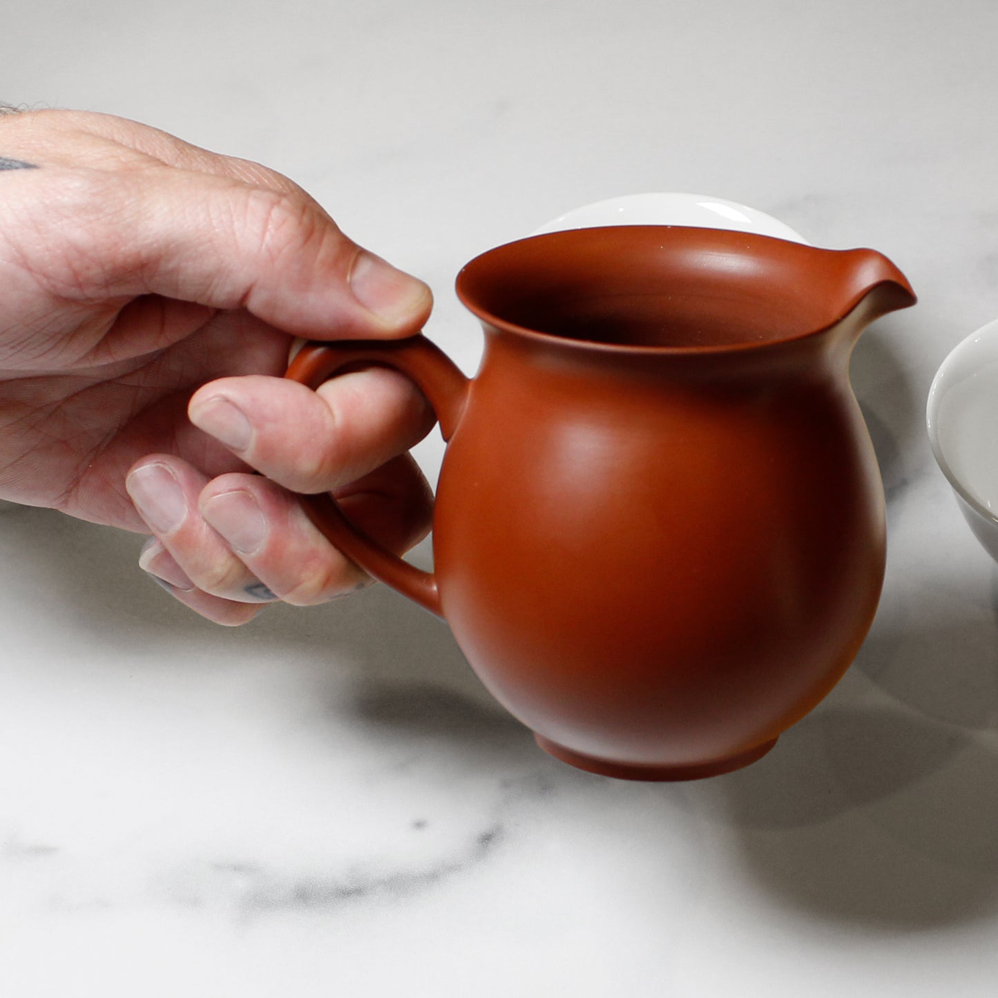 Hand holding a red ceramic pitcher on a marble surface