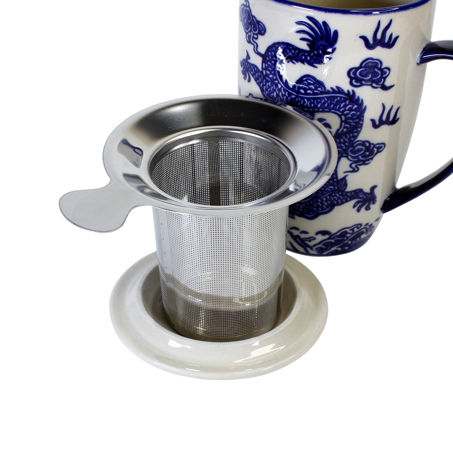 Stainless steel tea infuser on a white coaster with a blue and white mug featuring dragon design on a white background.