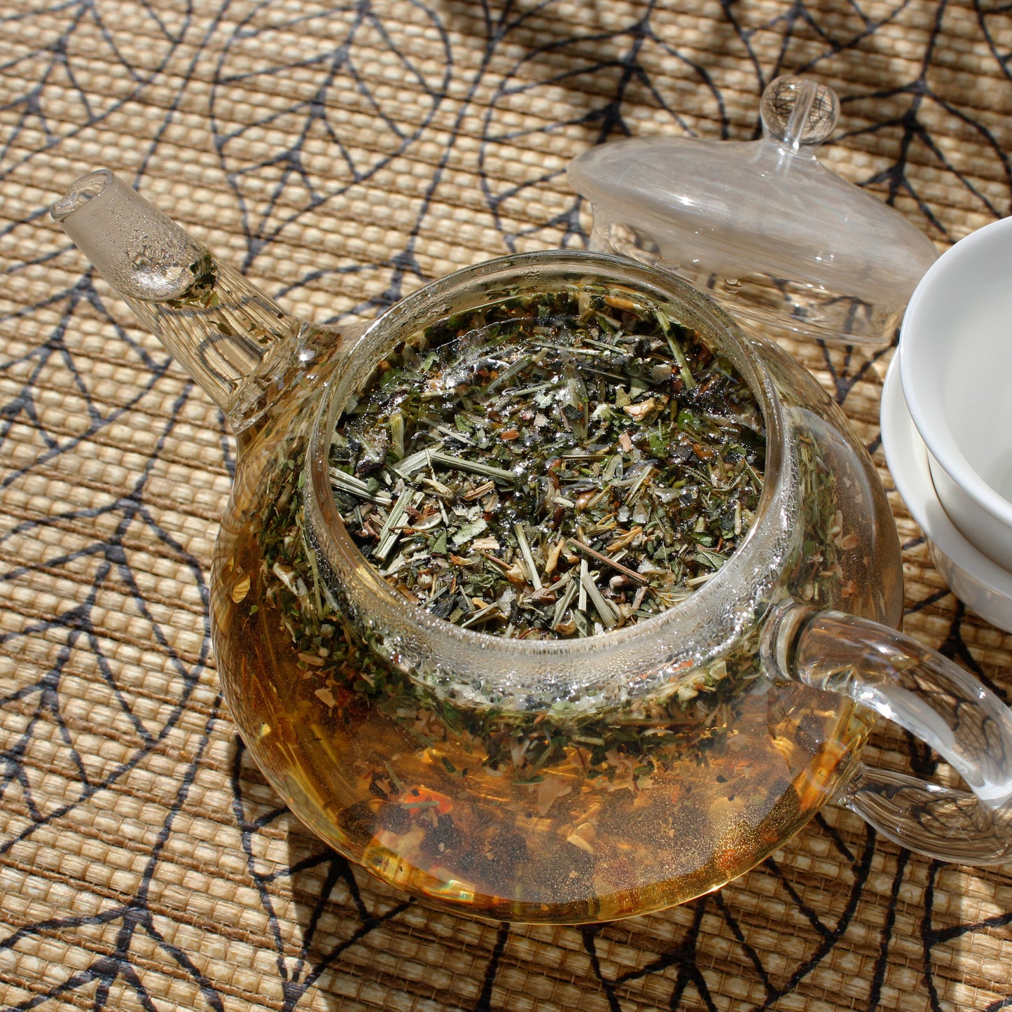 A glass teapot full of wet Herb Garden leaves and brewed tea sits on a leaf pattern table cloth. Tasting Notes:
thyme • mint • lemon verbena