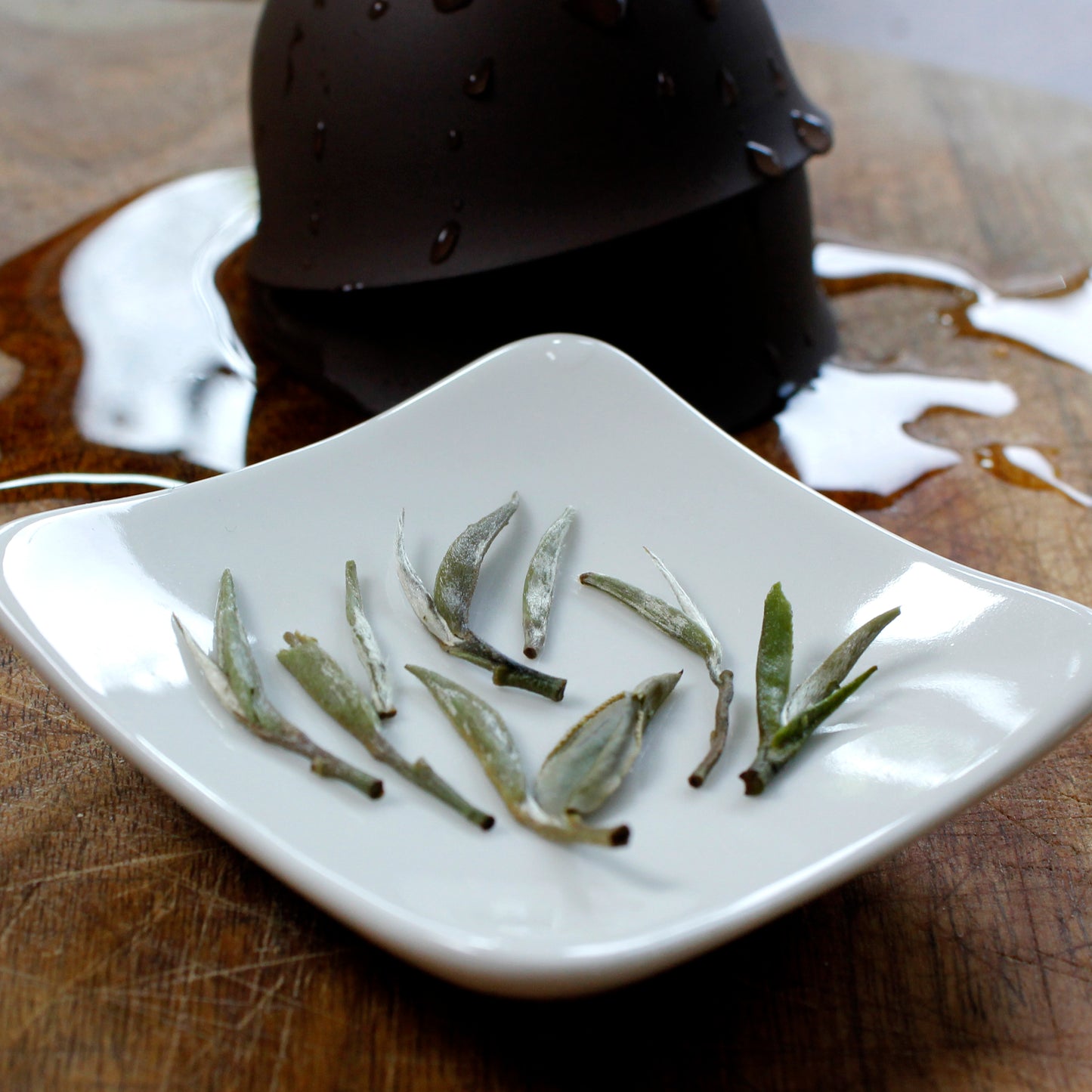 A few whole leaves on a dish with used cups in the background on a wet wood table. Tasting Notes:
clover • cucumber • white grape