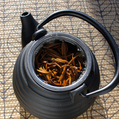 Black teapot with wet tea leaves on a leaf pattern brown table cloth.  