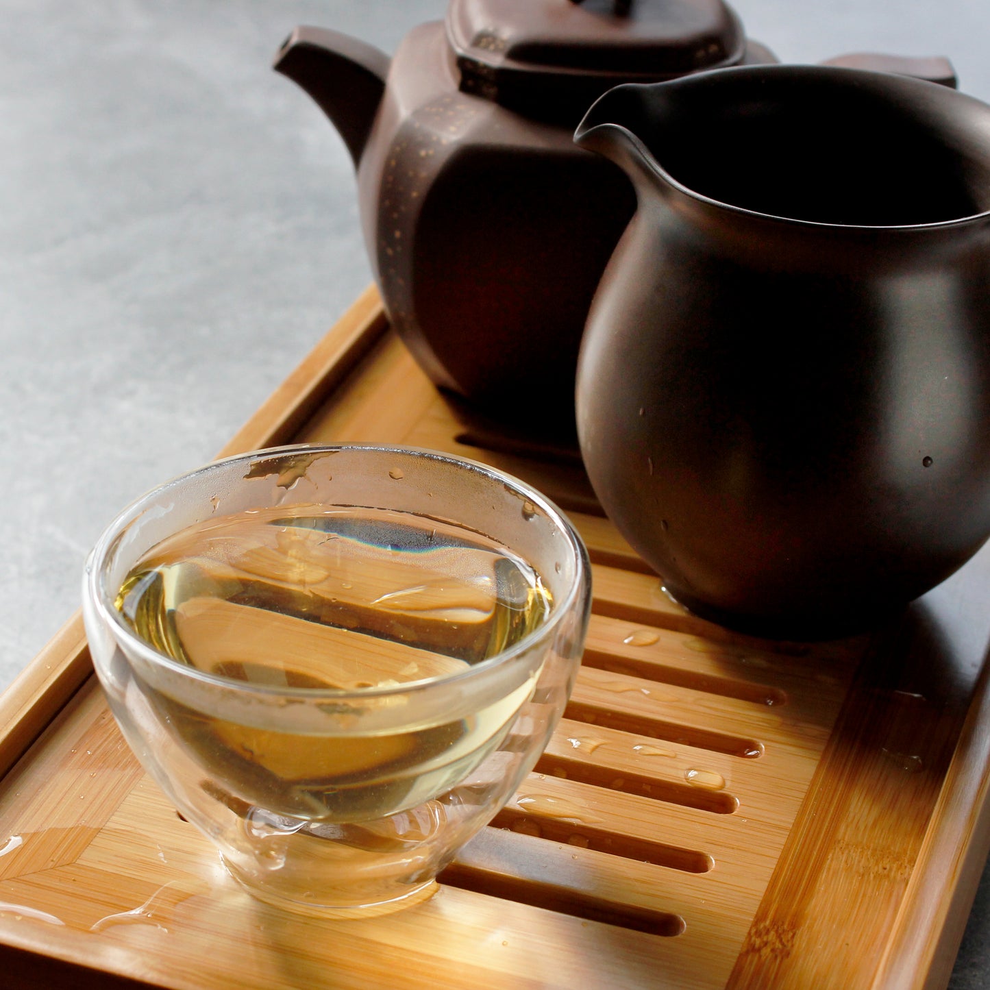 Bergamot Oolong - infusion in a glass tea cup, clay pitcher and teapot in back ground. Tasting Notes:
lilac • limoncello • verbena
