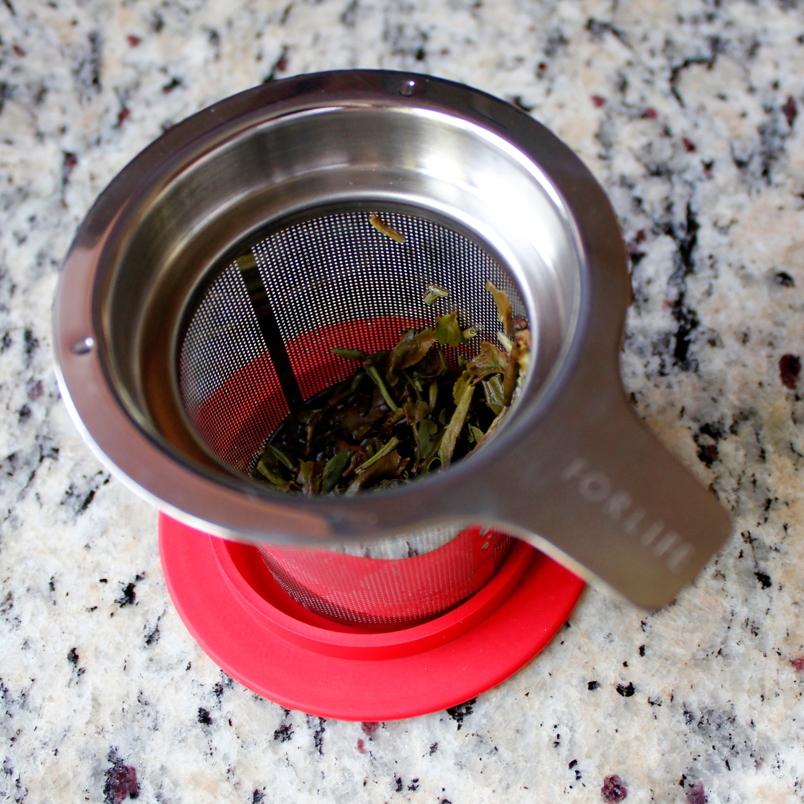 Tea strainer resting on the lid it comes with. Wet tea leaves are at the bottom, the lid catches any dripping tea. 