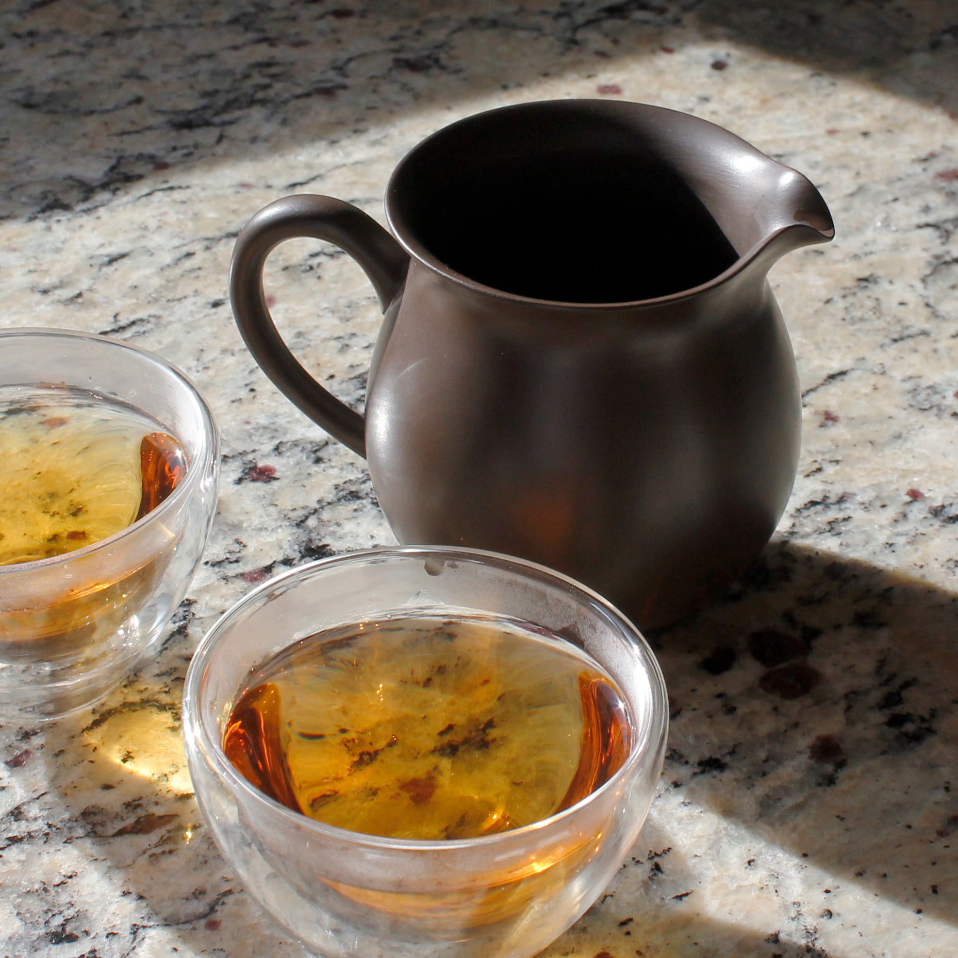 Classic clay pitcher shown with two glass tea cups filled with tea. 