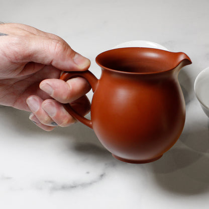 Hand holding a red ceramic pitcher on a marble surface