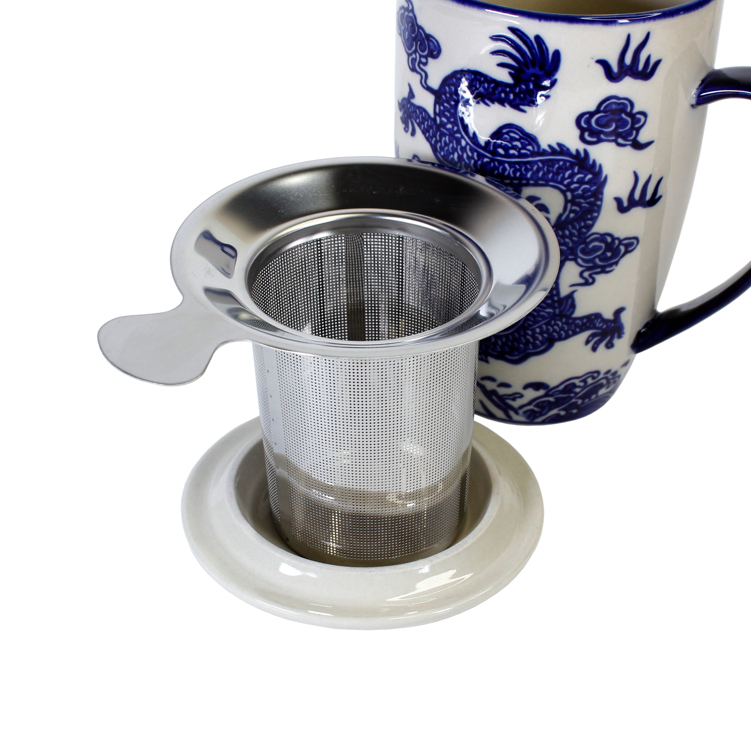 Stainless steel tea infuser on a white coaster with a blue and white mug featuring dragon design on a white background. 