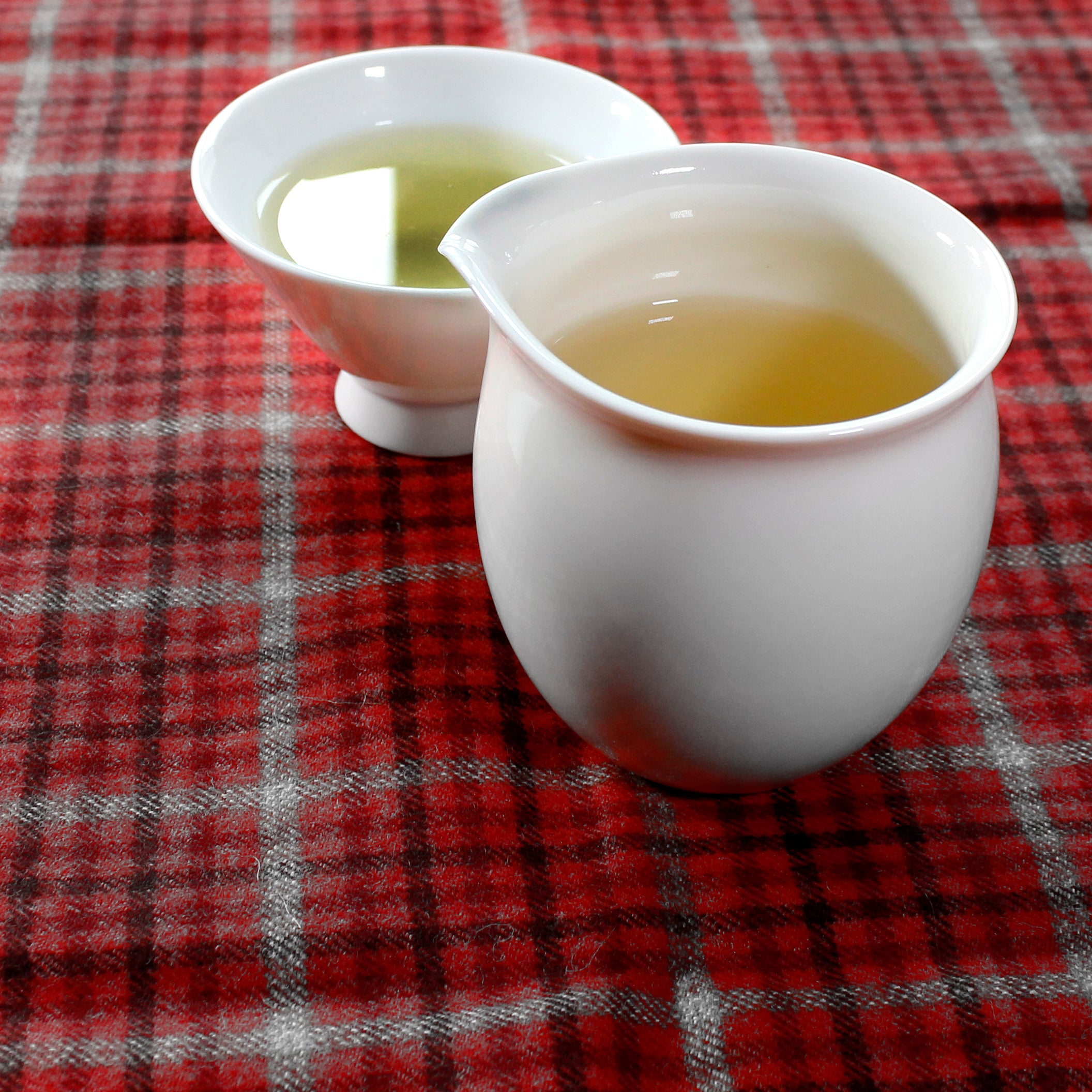 White Pitcher with matching tea cup, both filled with tea on a checkered red table cloth. 