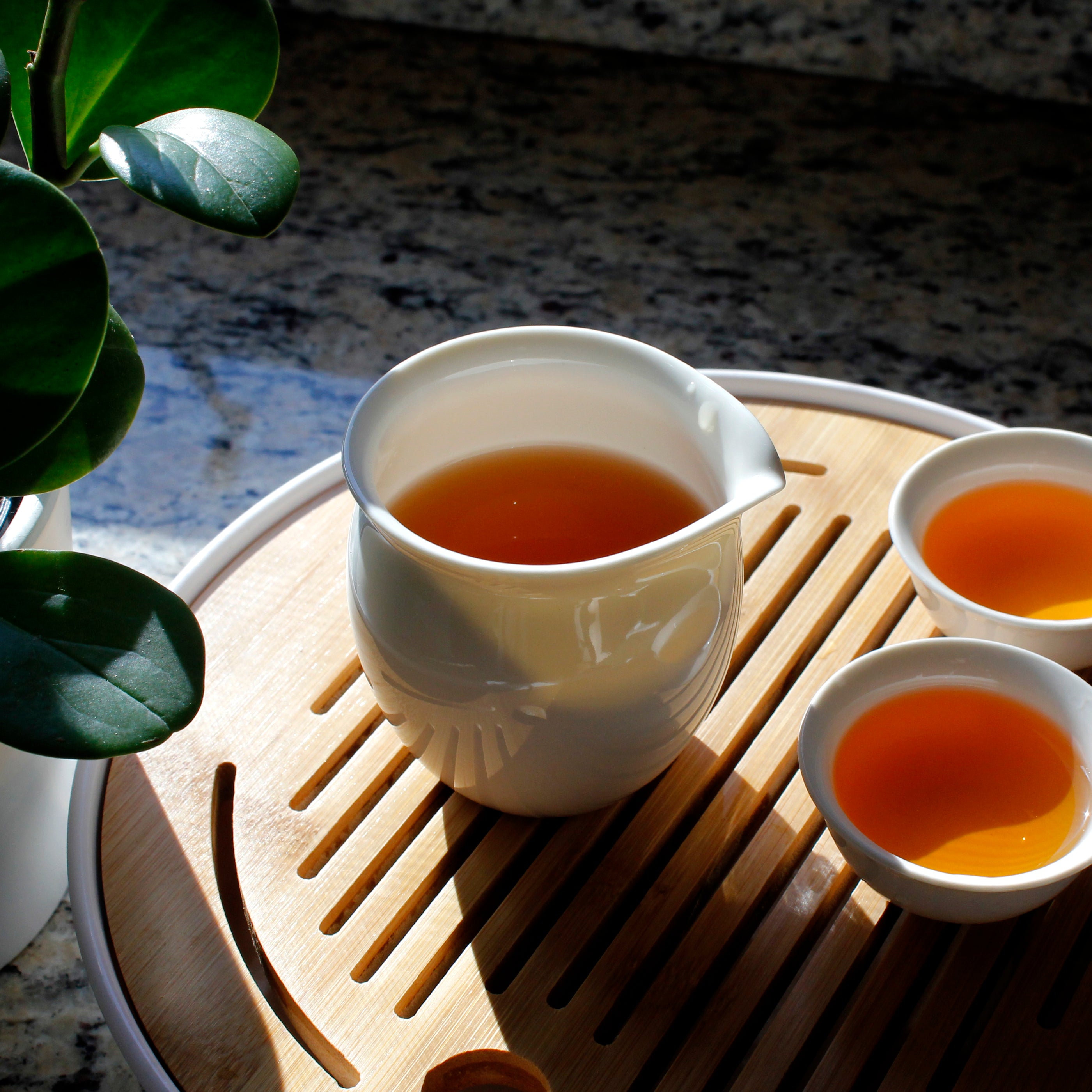 Pitcher with two matching tea cups filled with tea sitting on a bamboo tea tray. 