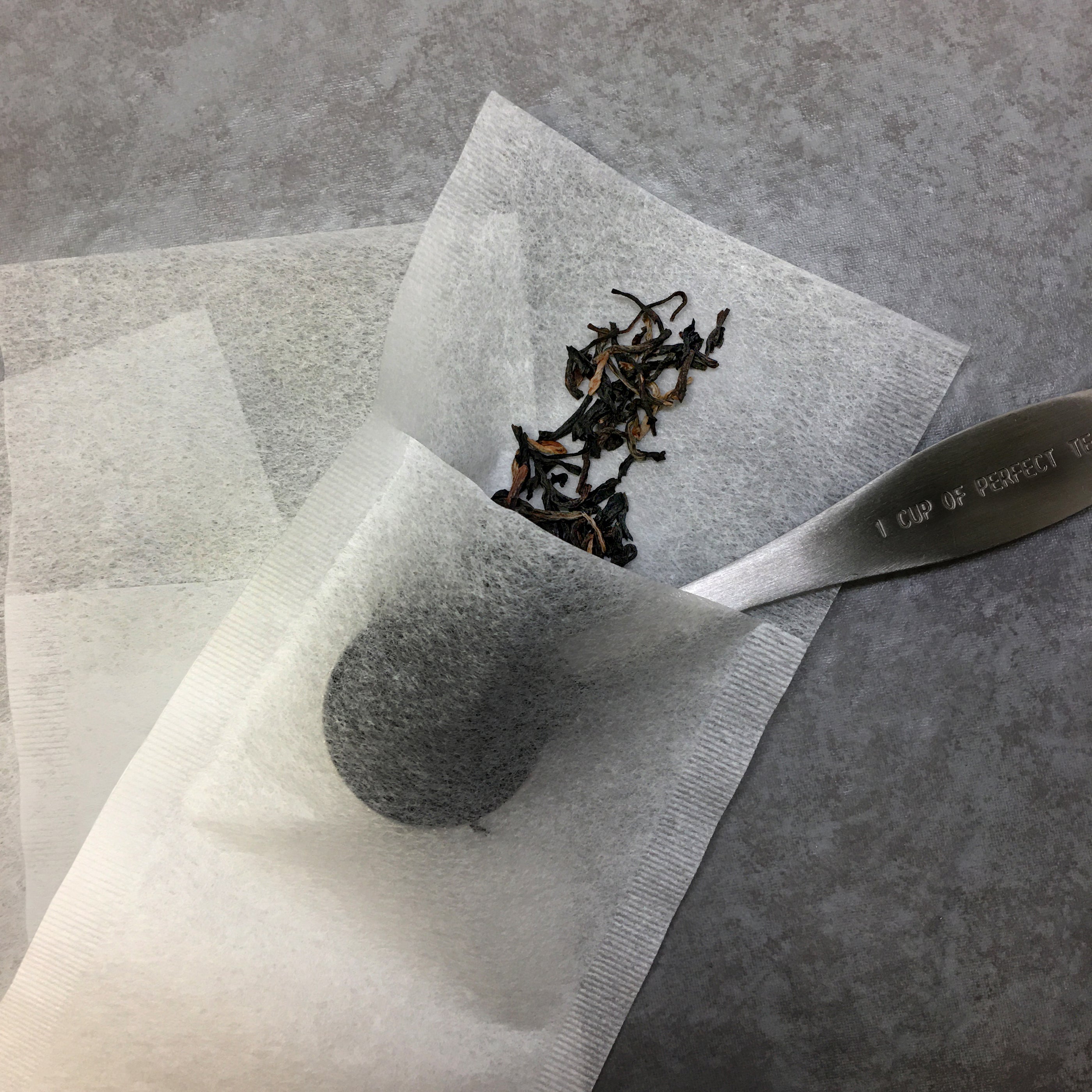 A tea scoop putting tea in the paper tea bag. 