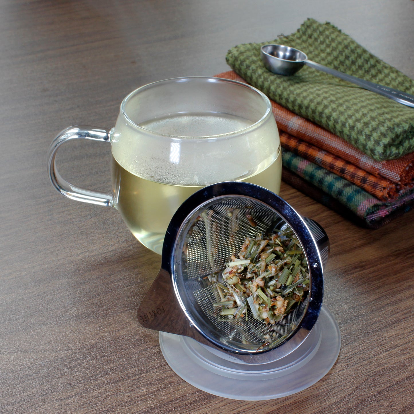 Ginger Lemon - wet leaves in a strainer placed on a coaster, Filled mug with cloth napkins and tea scoop. Tasting Notes:
honey • citron • ginger