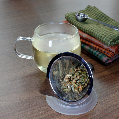 Ginger Lemon - wet leaves in a strainer placed on a coaster, Filled mug with cloth napkins and tea scoop. Tasting Notes:
honey • citron • ginger