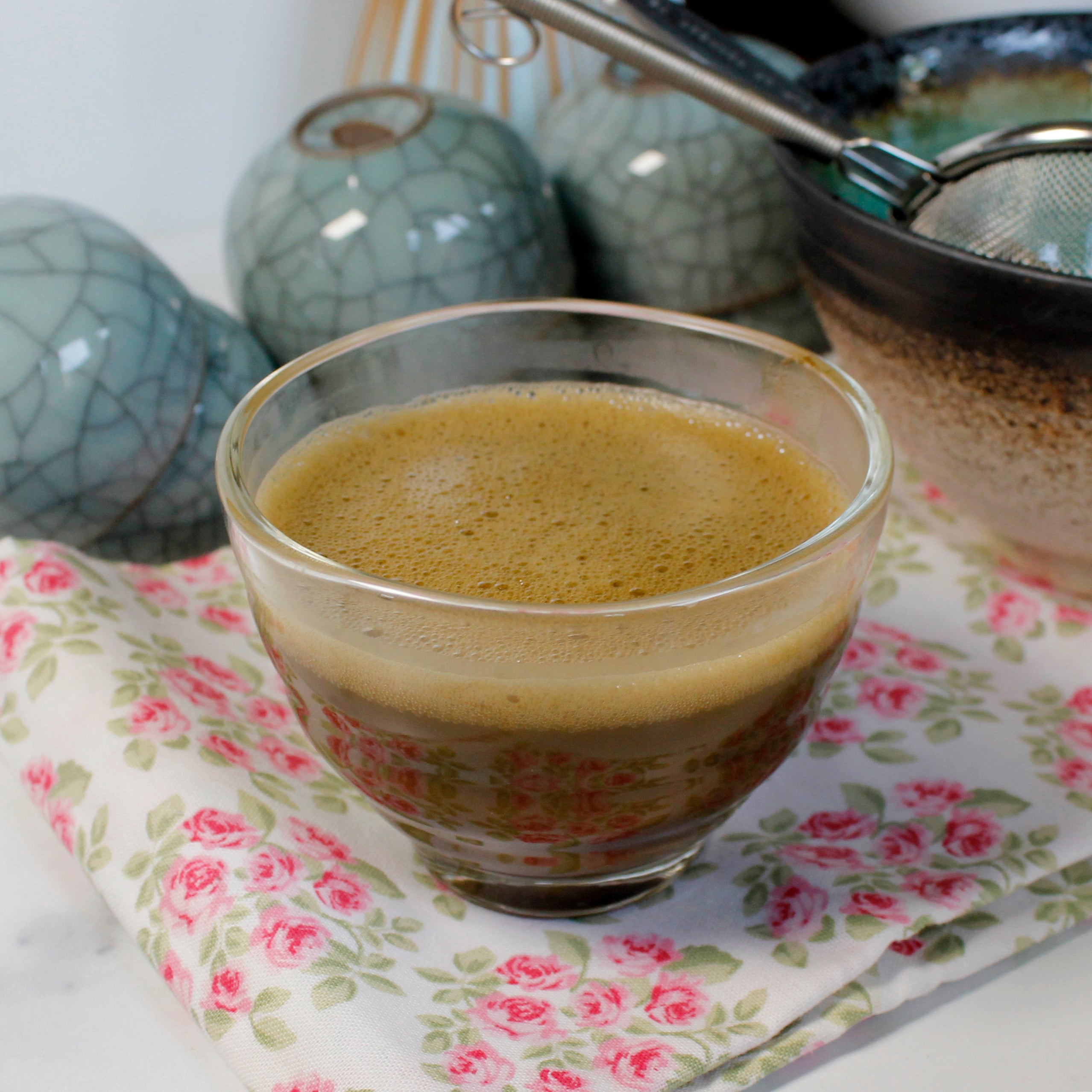 Hojicha  brewed in a glass cup on a rose print cloth, crackle blue teacups are in the background with other tea accessories. Tasting Notes:
chicory • peanut skin • roasted cacao