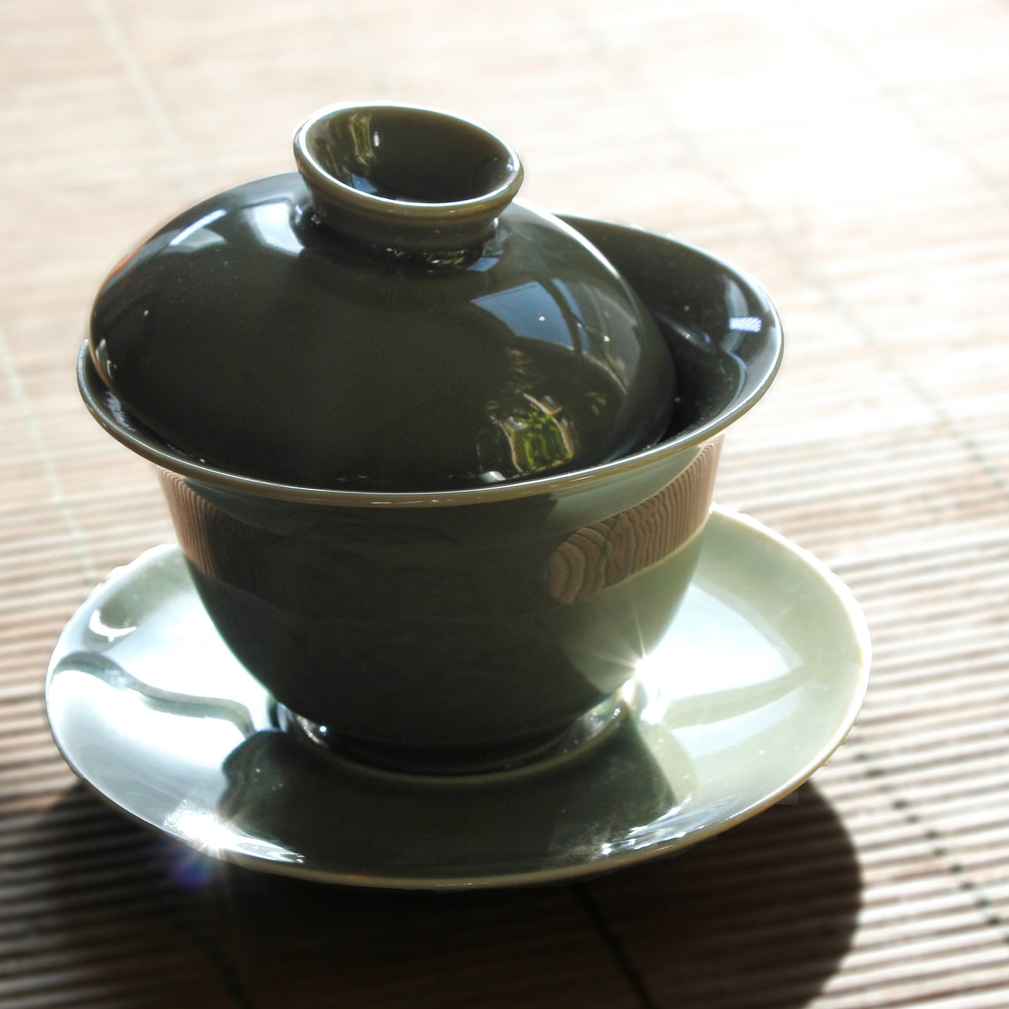 Green gaiwan on a bamboo mat in dark lighitng.