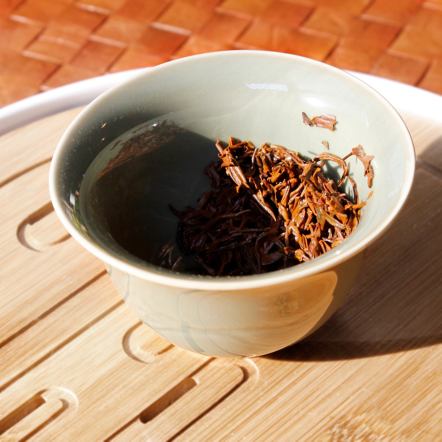 Wet leaves in a green gaiwan on a bamboo tray. 