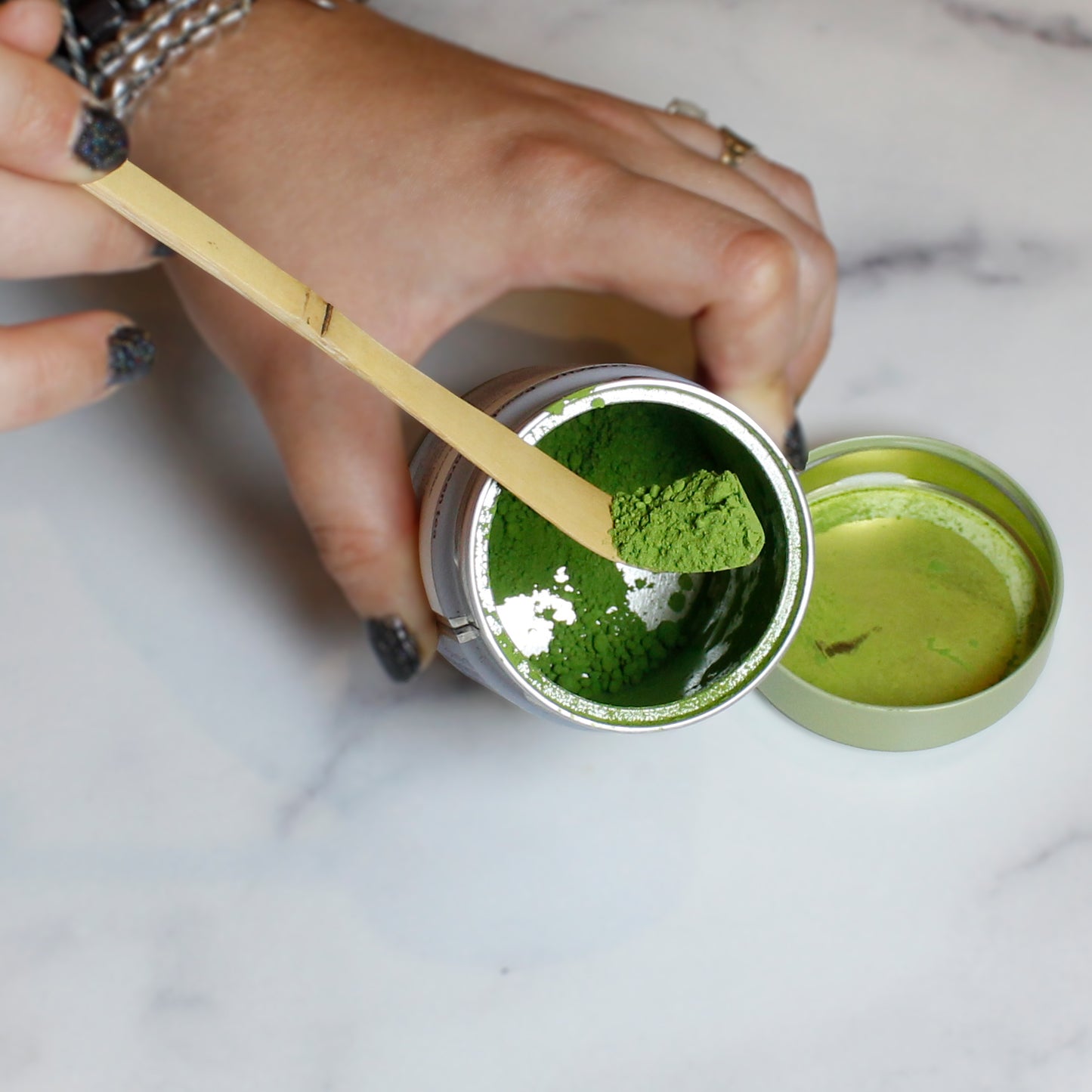 Person scooping green matcha powder from a container with a wooden spoon.