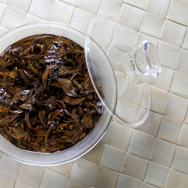 Sweet, fruity, and floral Oriental Beauty steeps in a glass gaiwan on a bamboo mat.