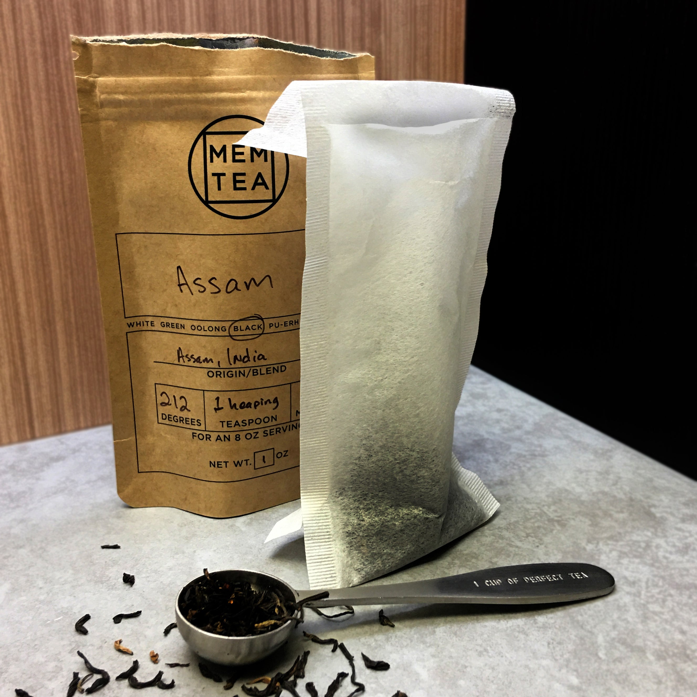 Tea scoop filled with ea in front of a tea sack and a tea bag of Assam black tea. 