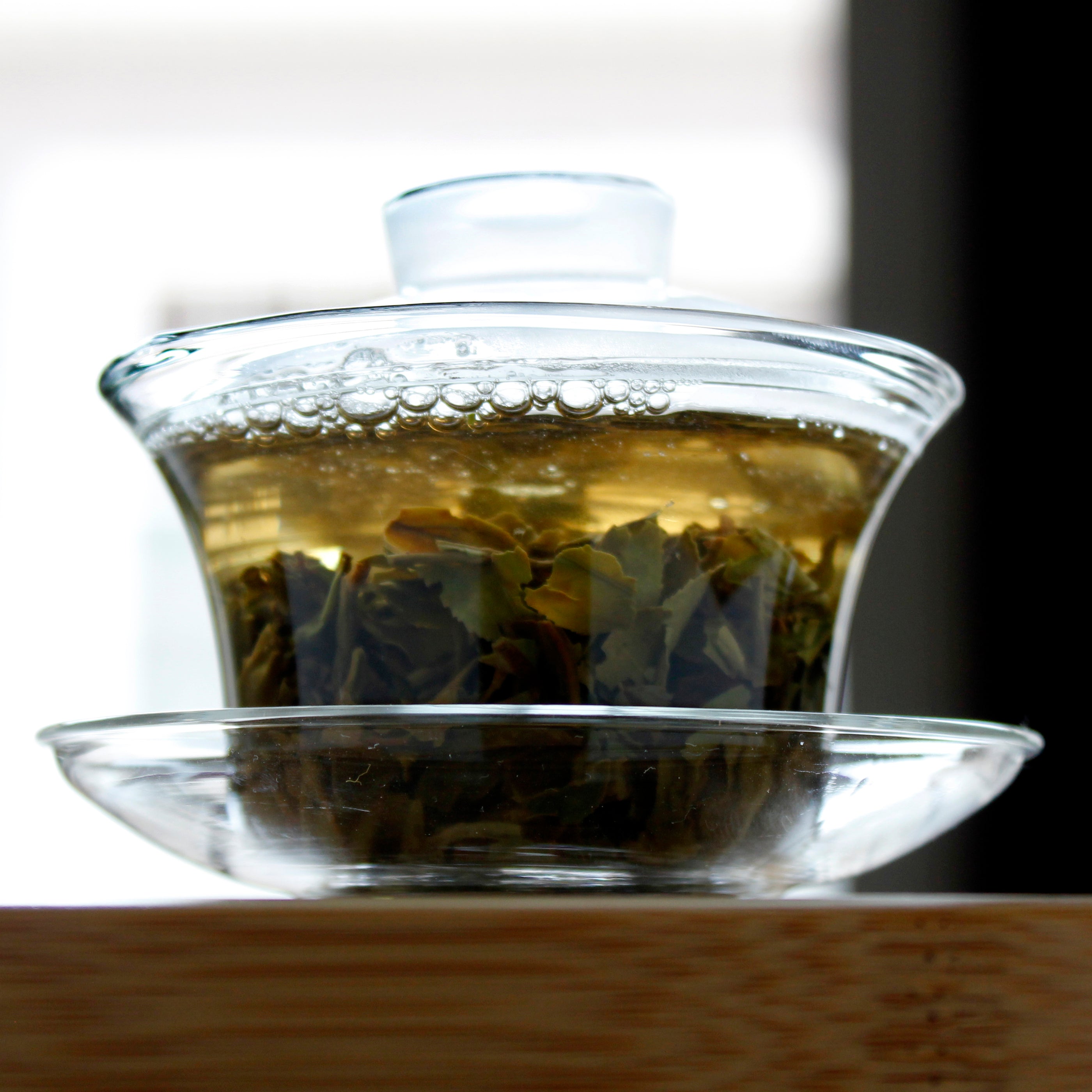 Gaiwan with tea and leaves, the water starting to turn a warm brown from the tea.